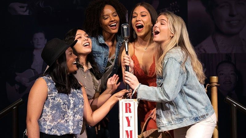 Photo of women posing with a mic stand on the stage of the Ryman