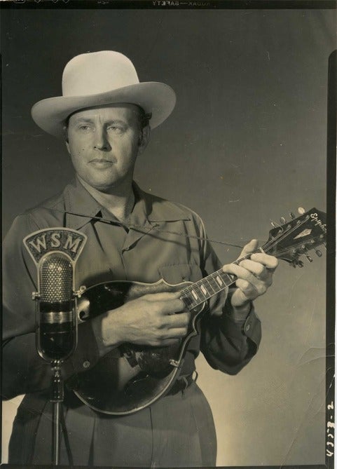 Bill Monroe with Epiphone mandolin posing in front of WSM mic.